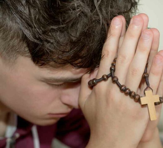 En person ber med ett radband och kors i händerna.